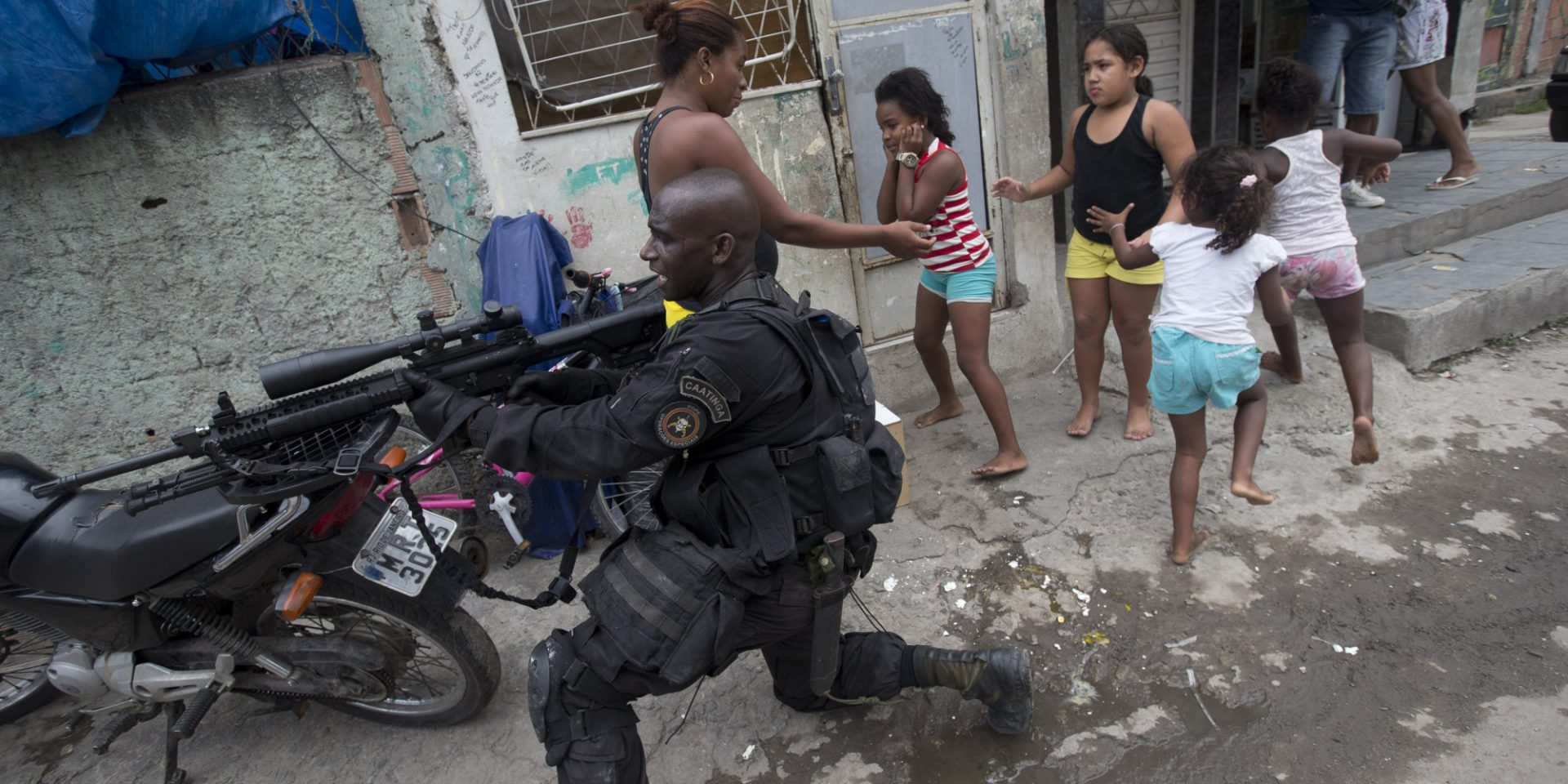 Special Police Operations Battalion (BOPE) officer takes position while residents run for cover during an operation in the Mare slum complex, ahead of its "pacification," in Rio de Janeiro, Brazil, Wednesday, March 26, 2014. 